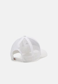 Gorra de béisbol blanca de malla con correa ajustable y pequeño logo colorido en la parte trasera, reposando sobre una superficie blanca lisa.