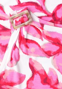 Gros plan d’un tissu floral rose et rouge avec une boucle rectangulaire beige attachée à une sangle.