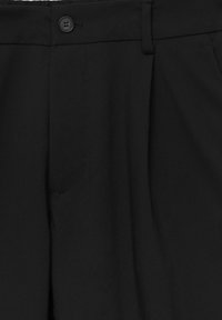 Pantalones negros ajustados con cierre de botón y trabillas para cinturón, mostrando la parte delantera de la cinturilla y parte de los bolsillos laterales.