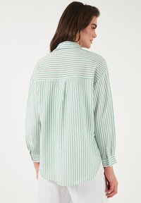 Green and white striped shirt with long sleeves, buttoned cuffs, and a back yoke detail. Lightweight fabric with a relaxed fit.