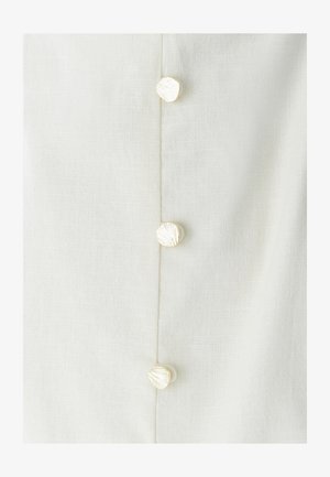 Približen posnetek kremaste tkanine s štirimi okroglimi, teksturiranimi belimi gumbi, ki so navpično poravnani po sredini.