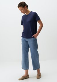 Marinelblauwe t-shirt met korte mouwen en een ronde hals, gecombineerd met lichtblauwe wijde jeans en beige platte schoenen. Eenvoudig en minimaal ontwerp.