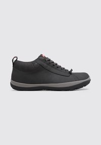 Zapatillas deportivas negras con parte superior suave, suela gris en contraste, punta redonda y detalles de costura sutiles. Incluye una lengüeta texturizada en el talón para facilitar su uso.