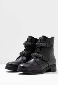 Botas de tobillo de cuero negro con punta redondeada, que cuentan con correas decorativas y hebillas, superficie texturizada y un tacón bajo en bloque.