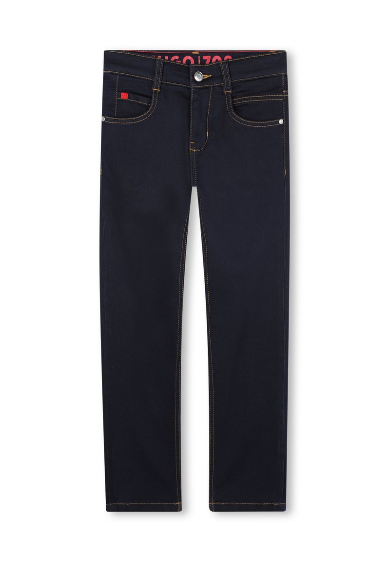 Jeans de mezclilla azul oscuro con costuras amarillas en contraste, cinco bolsillos y cierre de botón plateado. Presenta una etiqueta de marca roja en la cinturilla.