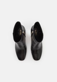 Botines de cuero negro con una textura suave, punta en forma de almendra, cremallera lateral pequeña y un sutil logotipo en la plantilla.