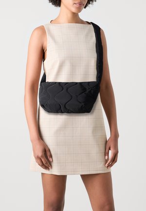 Borsa a spalla nera trapuntata con una texture ondulata, dotata di una tracolla, abbinata a un vestito senza maniche a quadri beige.