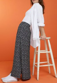 Pantalones de pierna ancha fluidos y estampados en un azul marino oscuro con diseños florales blancos. Combinados con una camisa blanca y zapatillas blancas.