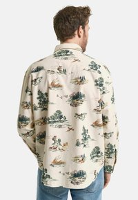 Langärmliges Hemd in Creme mit einem malerischen Muster aus Wäldern, Tieren und Bergen. Verfügt über einen abgerundeten Saum und einen knöpfbaren Kragen.