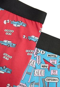 Primer plano de dos cinturillas de ropa interior con estampados de coches retro y el tema de la Ruta 66 en tela roja y azul con bandas elásticas negras.