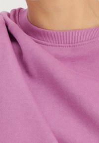 Sudadera de color púrpura claro con cuello de canalé y tejido suave y texturizado. La vista en primer plano muestra los detalles del tejido y la costura.