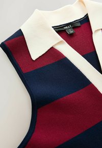 Débardeur en polo sans manches avec de larges rayures horizontales bleu marine, rouge et crème. Tissu texturé avec un col écarté. Étiquette de marque visible.