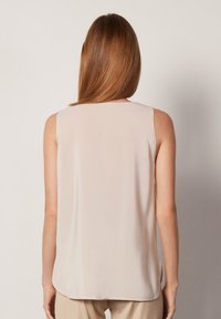 Ärmlös beige blus med ett mjukt, lätt tyg. Har en rund halsringning och en rak skärning som faller strax under midjan.