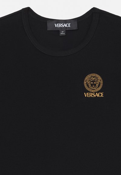 Svart Versace T-skjorte med rund hals, med en liten gyllen Medusa-hodelogo og "VERSACE"-tekst på venstre brystområde.