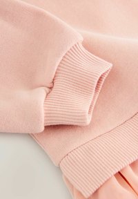 Roze katoenen sweatshirtstof met ribbels aan de manchetten en onderrand. Zachte textuur, close-updetail toont de stiksels en de stofweefsel.