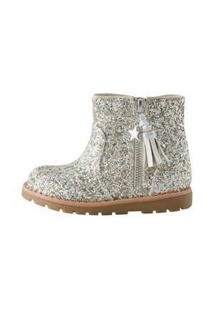 Kindersilberner Glitzergelenksschuh mit seitlichem Reißverschluss, Stern- und Quastenanhänger und brauner Gummisohle.