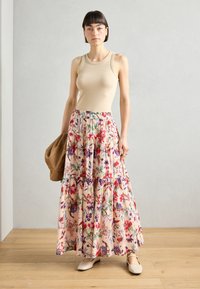 Canotta beige senza maniche abbinata a una gonna maxi a strati con motivo floreale in rosa, rosso e viola su uno sfondo chiaro.