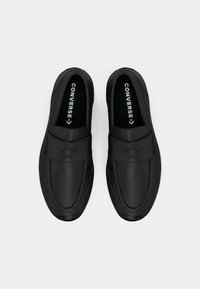 Svart slip-on-sko laget av glatt skinn, med en stjernegenerator på stroppen, rund tå og teksturert såle.