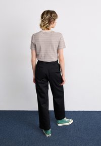 Grå og beige stripete kortermet skjorte sammen med svarte bukser og grønne joggesko. Enkelt design med løs passform og baklommer.