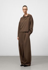 Maglione marrone, leggero e comodo, con un ampio colletto e dettagli con bottoni, abbinato a pantaloni a vita alta e gamba larga in tessuto coordinato.