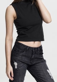 Un crop top sans manches noir avec un col montant, associé à un jean en denim foncé avec des détails déchirés et une silhouette ajustée.