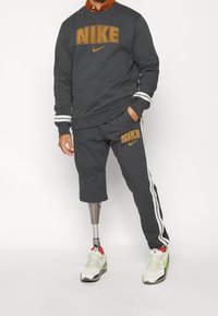 Sudadera y pantalones de chándal grises de Nike con logo naranja, rayas blancas en las mangas y en los pantalones, combinados con zapatillas blancas y verdes, que cuentan con una pierna prostética.