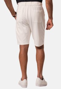 Shorts blancs texturés avec une taille élastique, dotés de deux poches arrière et d'une coupe droite, associés à des baskets blanches.
