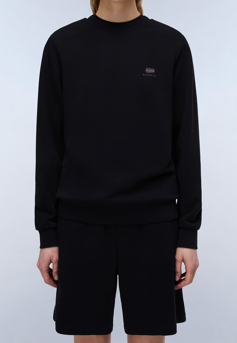 Personne portant un sweat-shirt noir à manches longues et un short noir assorti avec un petit logo sur le côté supérieur gauche du sweat-shirt.