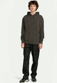 Kapuzensweatshirt aus dunkelgrauem Baumwollgemisch, mit einer Fronttasche und Kordeln. Kombiniert mit locker sitzenden schwarzen Hosen und Sneakers.