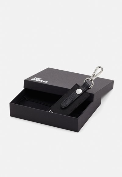 Portefeuille noir en cuir texturé et tissu, avec un clip en métal argenté et un bouton-pression, placé dans une boîte noire ouverte.