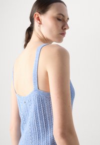 Lys blå strikket tanktop med brede stropper, som har et strukturert sikksakkmønster og en svakt åpen ryggdesign.