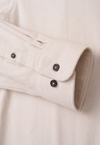 Light beige shirt cuff made of textured fabric, featuring two black buttons and visible seam details.