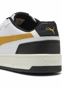Białe i czarne sneakersy z złotym paskiem akcentującym, wykonane z teksturowanej skóry i gumowej podeszwy. Logo umieszczone na pięcie.