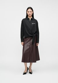Svart skjorte med knyttet søm, sammen med en burgunder imitert skinn midi-skjørt. Modellen har på seg svarte spisse hæler.