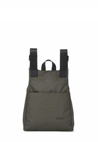 Mochila de tela color verde oliva con correas negras ajustables, asa superior y bolsillo delantero. Presenta un logotipo impreso en la parte inferior.