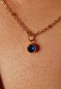 Gouden ketting met een ronde, gefacetteerde blauwe stenen hanger. Gladde textuur met een delicate sluiting geïntegreerd in het kettingontwerp.