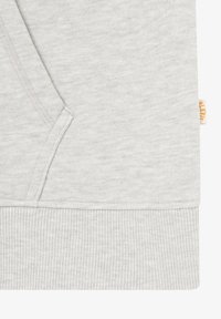 Tessuto grigio chiaro con tasca a marsupio e orlo a coste, con un piccolo'etichetta beige con testo arancione sulla cucitura laterale.