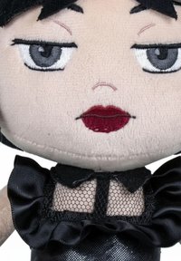 Poupée en peluche à la peau claire, cheveux noirs et yeux gris. Présente des lèvres rouges, un voile en maille et des accents en tissu noir froncé sur un corps brillant.