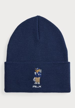 Bonnet en tricot bleu marine avec un revers, présentant un ours brodé portant une veste de club bleue et tenant des clubs de golf au-dessus du texte "RLX".