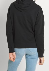 Czarna bluza z kapturem o luźnym kroju, z prążkowanymi mankietami i dolnym wykończeniem, pokazana od tyłu. Materiał wydaje się miękki o gładkiej teksturze.