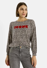 Camiseta de manga larga con estampado de leopardo y texto rojo "ICON", confeccionada en tela suave; combinada con jeans grises de talle alto.