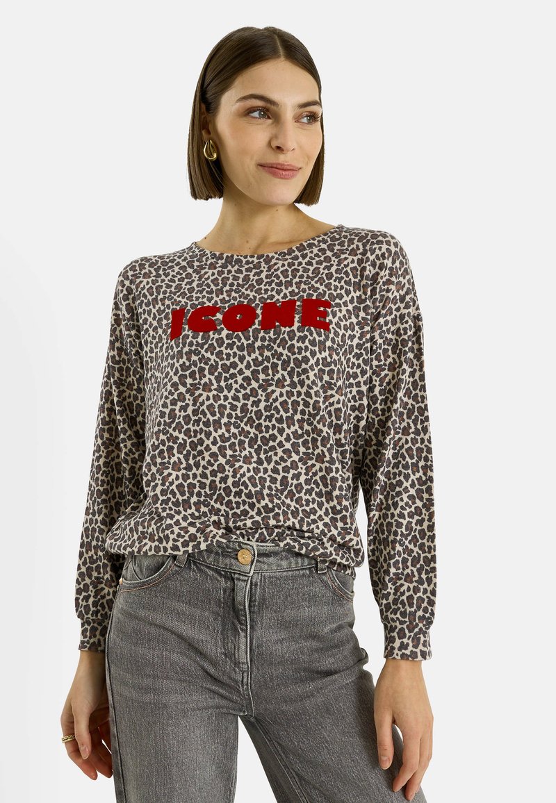 Camiseta de manga larga con estampado de leopardo y texto rojo "ICON", confeccionada en tela suave; combinada con jeans grises de talle alto.