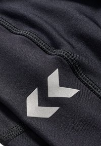 Zwart sportstof met een gestructureerd oppervlak, voorzien van een contrasterend zilveren chevronlogo en zichtbare stikdetails.