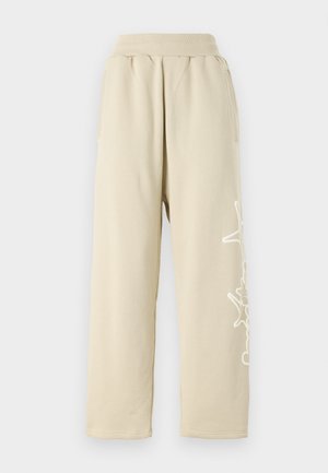 Beige Sweatpants mit lockerer Passform, einem elastischen Bund, Seitentaschen und einem weißen grafischen Detail entlang des linken Beins. Aus weichem Baumwollmaterial.