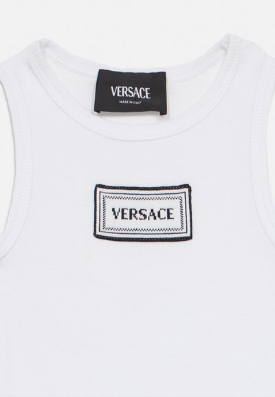 Witte mouwloze top met een zwart-witte Versace-logo patch op de borst en een zwart Versace-label dat binnenin de halsnaad is genaaid.