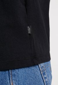 Sort bomulds T-shirt med et lille mærke på siden, parret med lyseblå denimjeans. Glat tekstur og enkelt design.