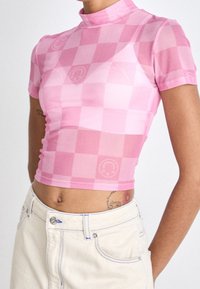 Krátký růžový kostkovaný crop top s vysokým límcem a krátkým rukávem, vyrobený z lehkého, elastického materiálu. Obsahuje jemné loga.