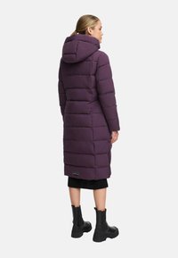 Abrigo acolchado púrpura con capucha, que presenta un diseño largo, textura acolchada en forma de cuadrícula y un lateral con cremallera con un acento de marca en el dobladillo.