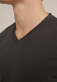 Camiseta gris oscuro con diseño de cuello en V, hecha de una tela suave, que muestra un primer plano del escote y la textura.