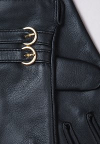 Black leather gloves with two gold circular hardware accents and subtle stitching details. Smooth texture with a fitted design and plush lining.